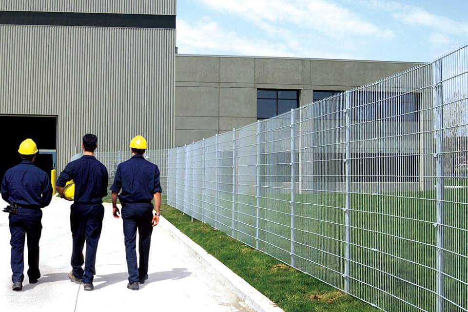 Three workers are walking towards the warehouse surrounded by 358 high security fence.