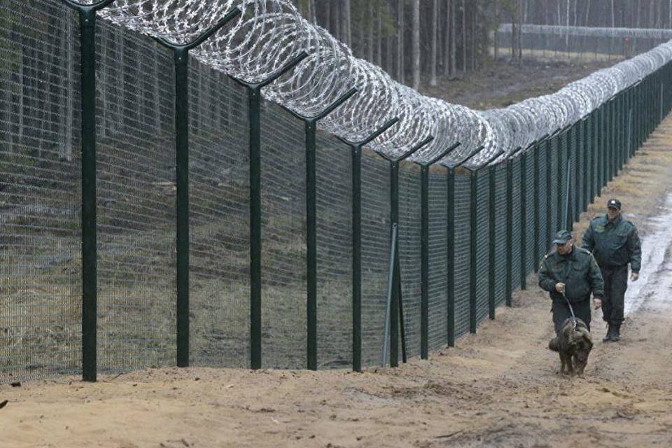 Two soldiers and a dog are walking along 358 security fence with a concertina topping.