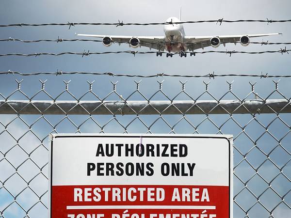 An airplane is flying over the chain link fence equipped with barbed wires.