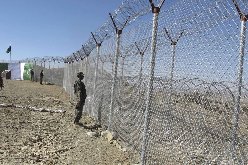 Soldiers are standing along the chain link fence with a concertina topping.