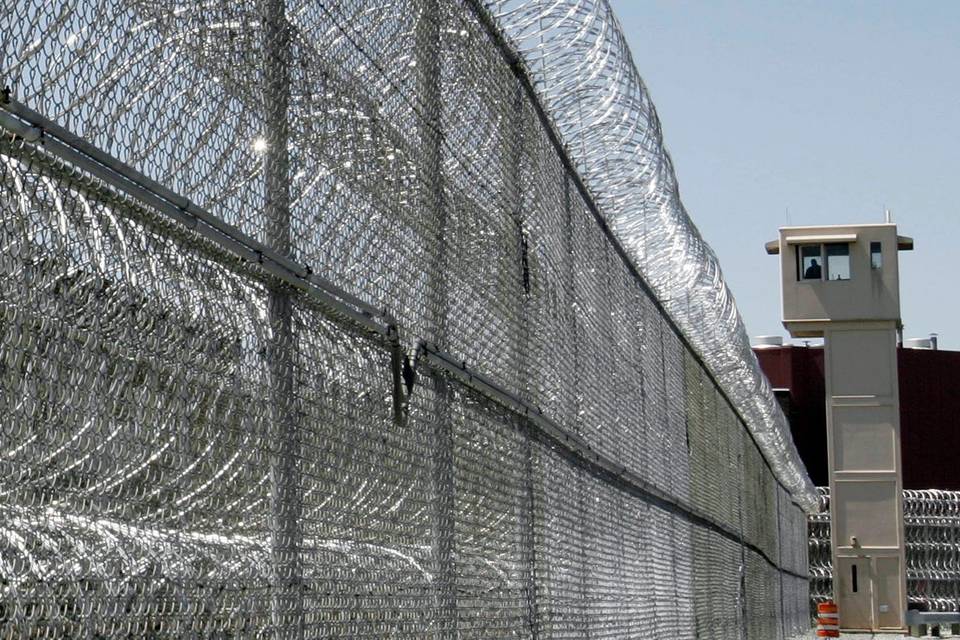 The prison watch tower is enclosed by chain link fence with razor wires.