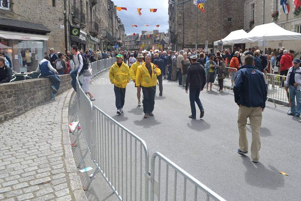 Many people are walking on the street that placed crowd control barrier on both sides of the street.