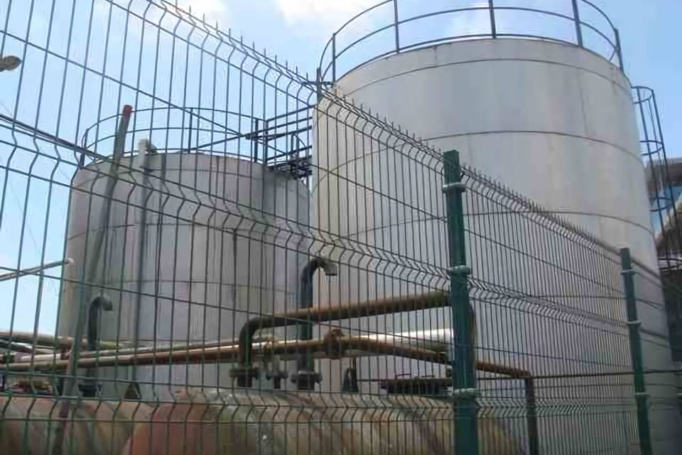 Two huge oil & gas tanks are stored in the yard enclosed by curvy welded fence.