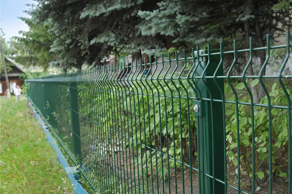 Many trees and plants are planted in a park enclosed by curvy welded fence.