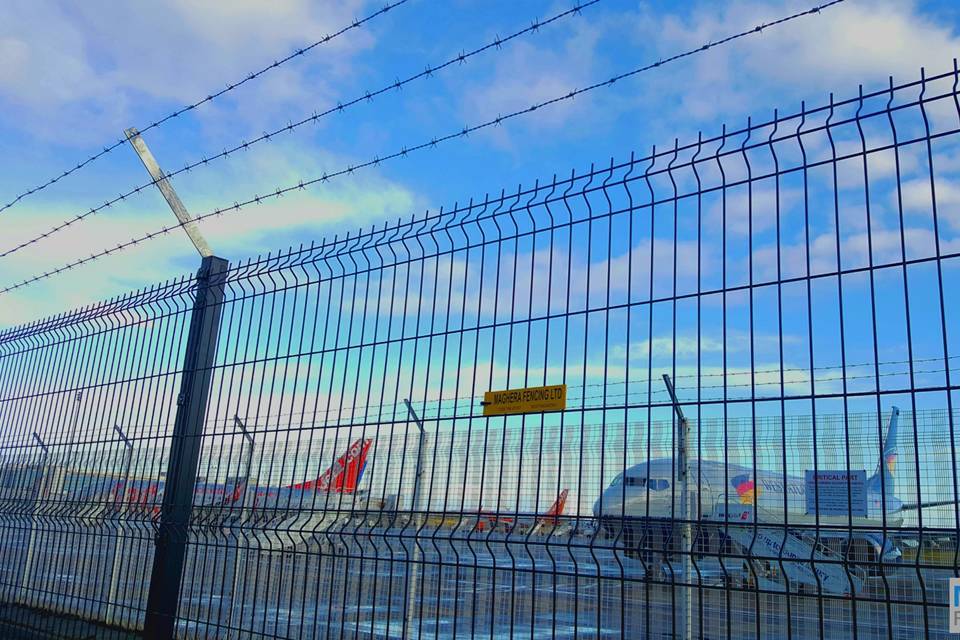 Green curvy welded mesh fences with barbed wires are installed in the airport