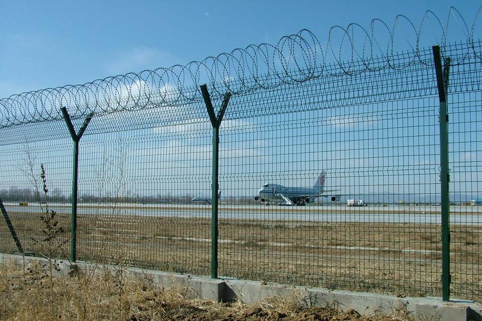 Green curvy welded mesh fences with razor wires are installed in the airport.